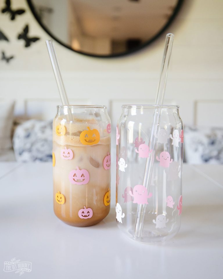 Two beer can glasses decorated with little cricut cut outs of orange pumpkins and pink and white ghosts.