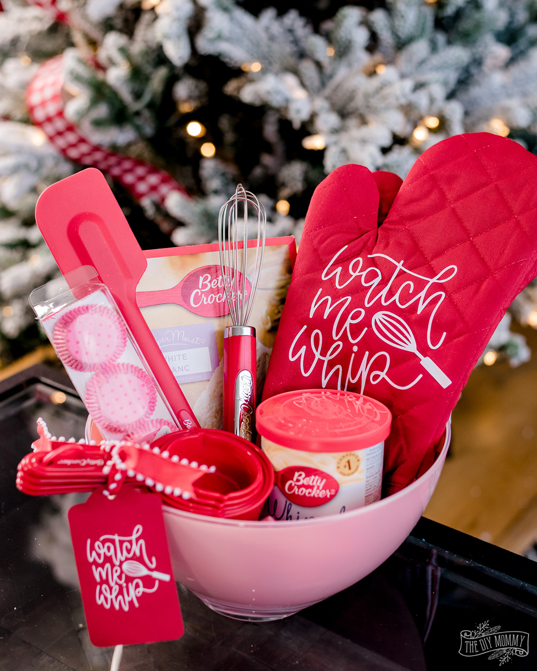 Baking themed gift basket filled with measuring cups, whisk, spatula cake mix, icing and a personalized red oven mitt. 